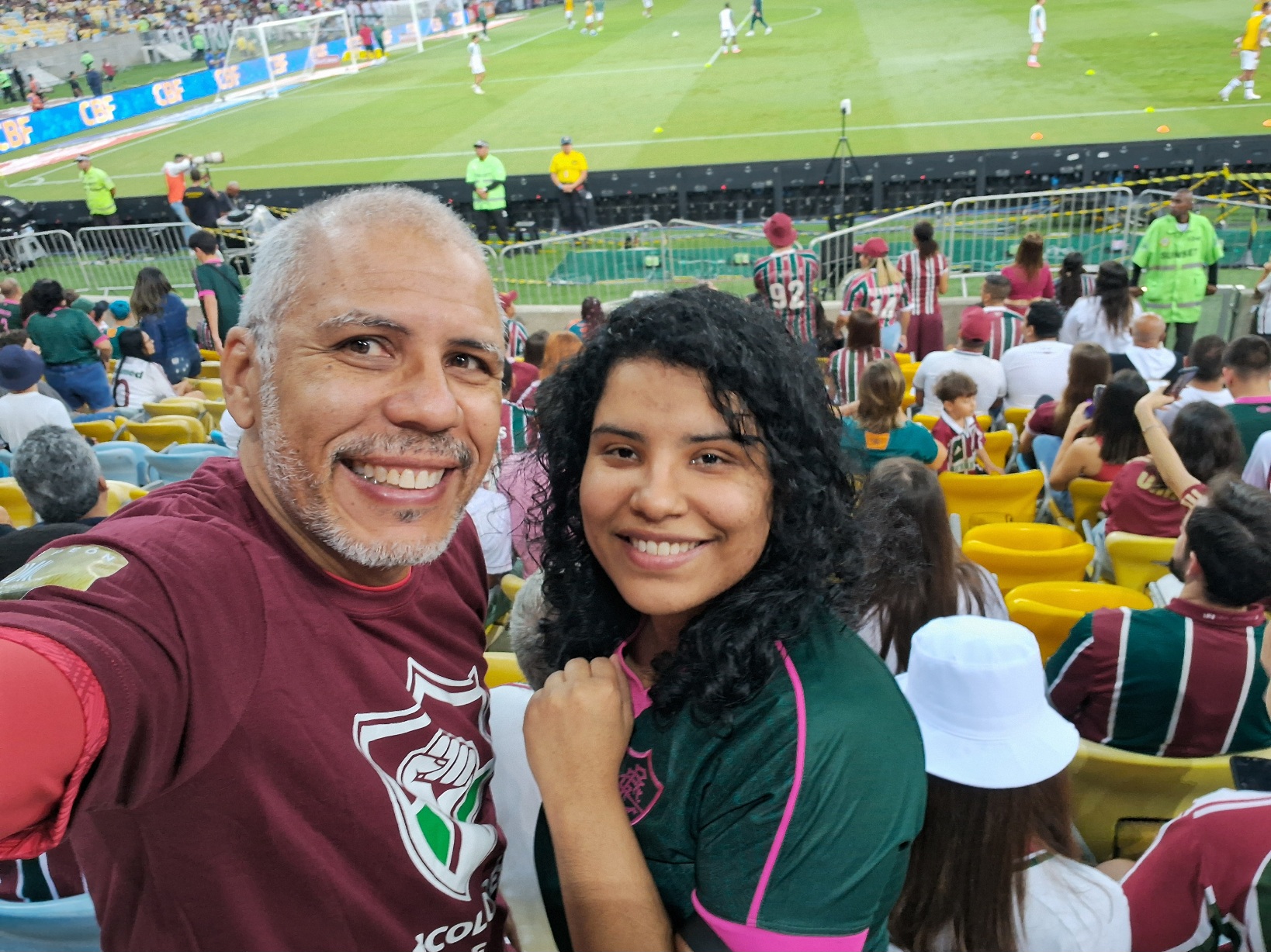 foto: Eu com camisa dos tricolores de esquerda ao lado da minha filha, com camisa do fluminense, nas arquibancadas do Maracanã, estamos sorrindo para a foto, ao fundo o campo