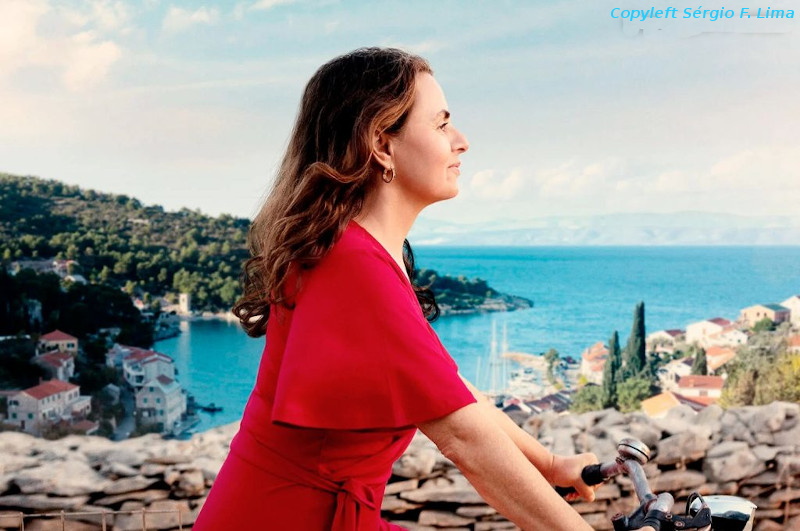 Foto da Zeynab, protagonista do filme "Em uma ilha bem distante", de vestido vermelho, andando de bicicleta, com o mar ao fundo