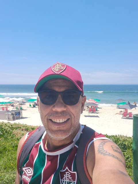 Autorretrato em que estou de camiseta e bon do Fluminense, de culos escuros no primeiro plano. Ao fundo a praia da Barra da Tijuca!