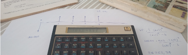 Imagem de uma calculadora HP12C sobre uma folha com resoluções escritas à mão.